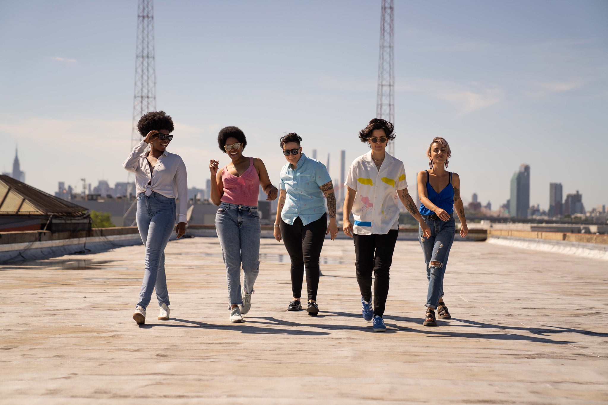 Group of women and folks with short hair walking towards the camera on a rooftop on a sunny day