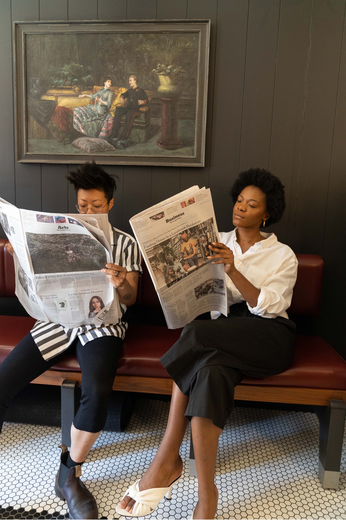 Asian short-haired person and black woman with fro reading newspapers in Barbershop waiting room